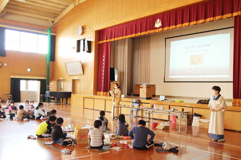 福岡市内の小学校での博多人形絵付け体験教室です。講師の博多織師、宮嶋美紀が全体の説明しています。